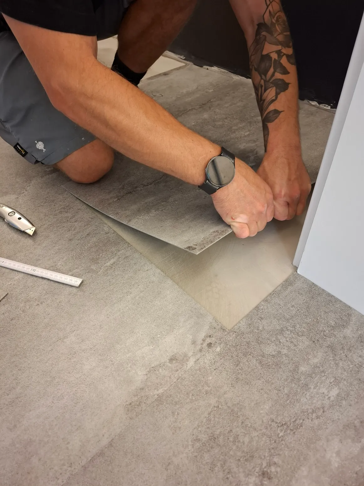 Designbelag verlegen in Fliesenoptik Handwerker verlegt Designbelag in Fliesenoptik am Türrahmen