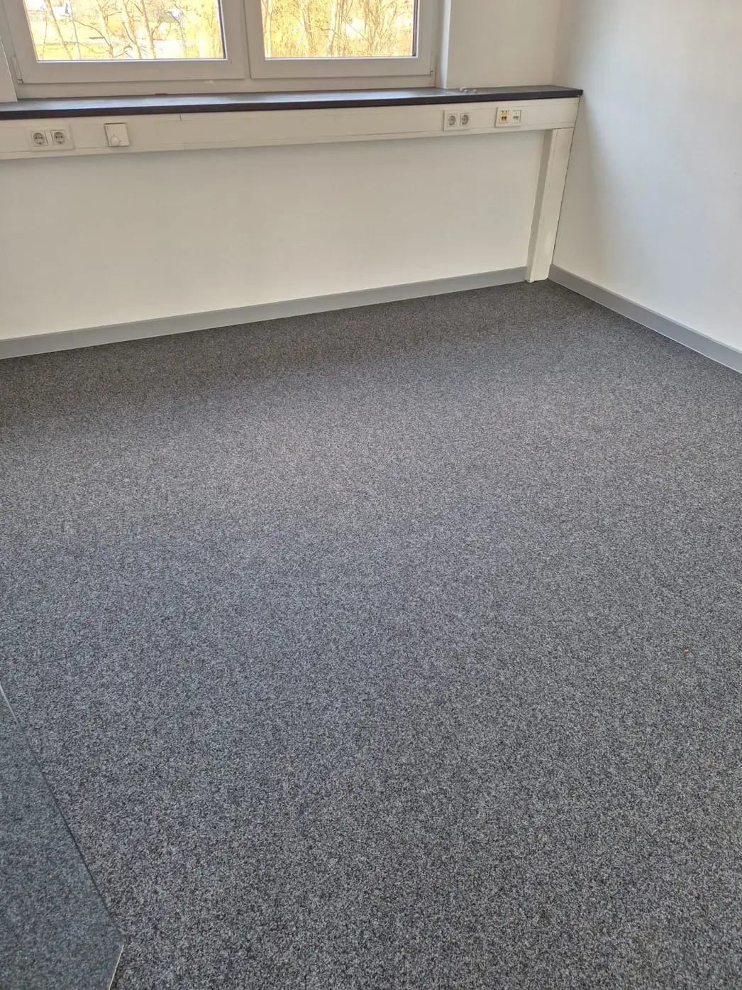 Grauer Teppichboden in Raum mit Fensterbank